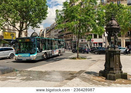 PARIS, FRANCE - MAY 25, 2016: Wallace fountain, public bus and cars on the street of Paris - capital and largest city of France it is also one of the popular travel destinations.