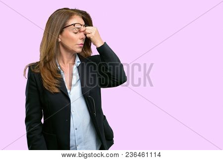 Middle age business woman with sleepy expression, being overworked and tired, rubbes nose because of weariness