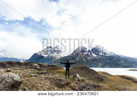 Woman Standing With Arm Wide Open With Torres Del Paine Mountain Range In The Background.