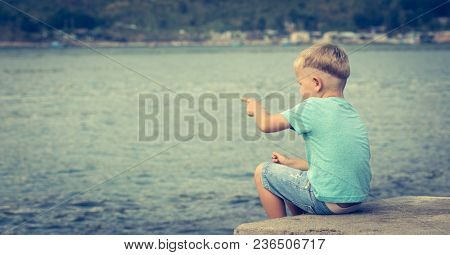 Cute caucasian boy pointing at seaside. Rear view. Leisure time