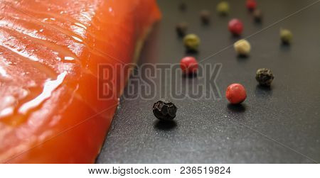 Trout Slice With Drops Of Oil And Scattered Black, Red And Green Pepper On A Dark Background