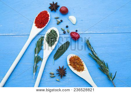 Cooking Hot Spicy Food Concept. Dry Spices And Herbs In Wooden Spoons, Fresh Herbs And Cherry Tomato