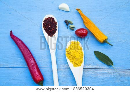 Cooking Hot Spicy Food Concept. Dry Spices And Herbs In Wooden Spoons And Chili Peppers On Blue Wood