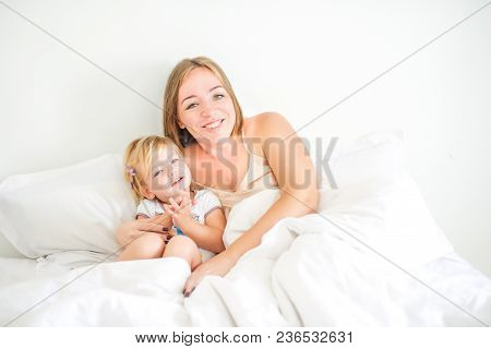 Happy And Loving Mother Having Fun And Embrace Her Daughter On The Bed. Family Morning Concept. Spen