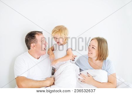 Happy And Loving Family Morning Concept. Cheerful Parents In Sleepwear Having Fun With Their Daughte