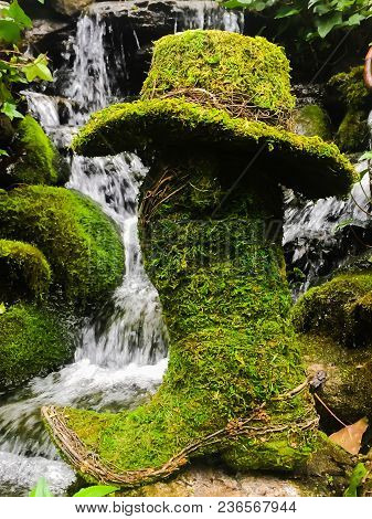 A Moss Covered Boot And Hat Sitting In Front Of A Lush Green Tranquil Waterfall