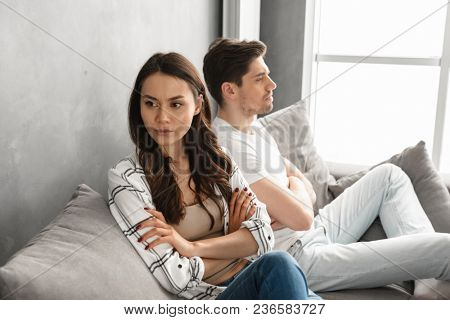 Photo of resentful guy and girl acting like arguing couple and not speaking to each other, while sitting together on couch at home isolated over white background