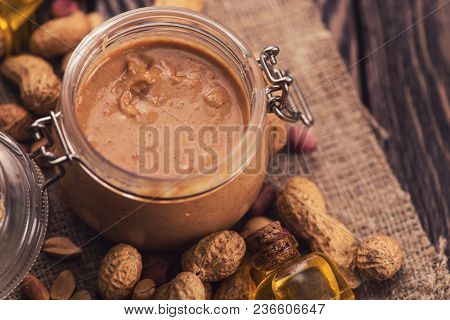 Natural peanut butter with oil in a glass jar and peanuts