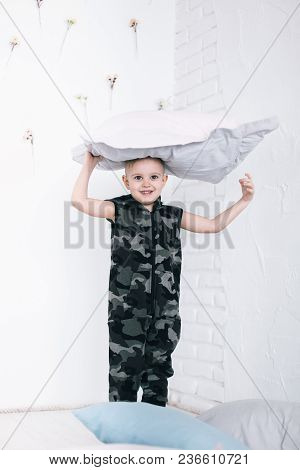 Smiling Little Boy. Emotional Blonde-hair Boy Standing In A Pillow Over His Head. White Floral Wall 