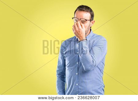 Handsome middle age man with sleepy expression, being overworked and tired, rubbes nose because of weariness