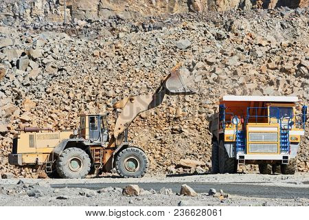 Granite mining. Wheel loader loading ore into dump truck at opencast