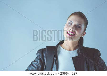 portrait of beautiful young brunette woman in stylish black jacket on gray.