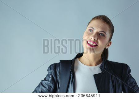 portrait of beautiful young brunette woman in stylish black jacket on gray.