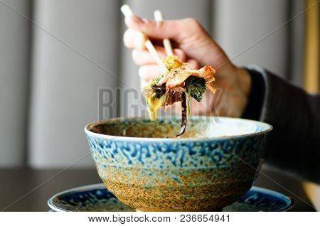 Man's Hand Holding Chopsticks Over A Plate Of Japanese, Thai, Chinese Meal - Rice, Mushroom, Vegetab