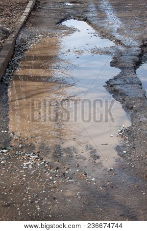 Dangerous Destroyed Roadbed. The Bad Asphalted Road With A Big Pothole Filled With Water. Mirror Ref