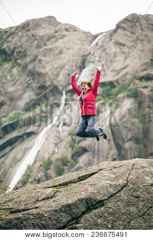 Happy Woman Jumping On Rock In Grey Mountains, Enjoying Traveling And Adventure.