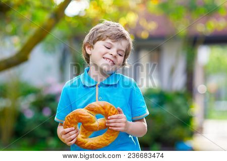 Adorable Little Kid Boy Eating Huge Big Bavarian German Pretzel. Happy Blond Child Enjoying Tasteful