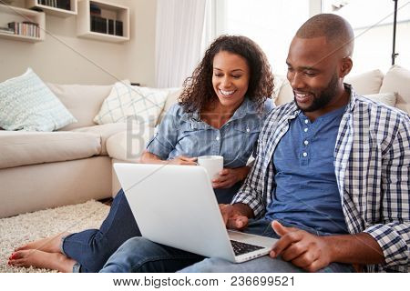 Young black couple using laptop sitting on the floor at home