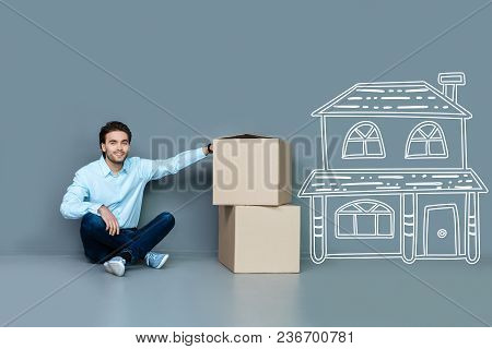 Dreams Come True. Emotional Young Positive Man Feeling Happy While Sitting On The Floor In His New W