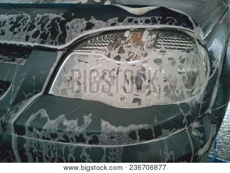 Car Wash. Soap Foam Dissolved Dirt On The Left Front Headlight Of The Car