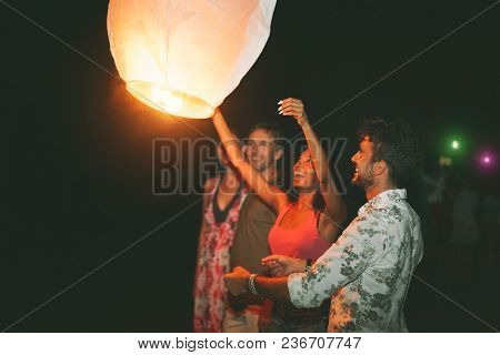 Happy Friends Lighting Sky Lantern On The Beach In The Night - Young People Having Fun In Asian Floa