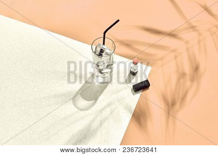 High Angle View Of Lipstick And Drinking Glass With Ice On Table. Beige And White Background With Sh