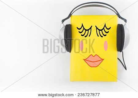Audiobook On White Background. Headphones Put Over Yellow Hardback Book, Empty Cover, Copy Space For