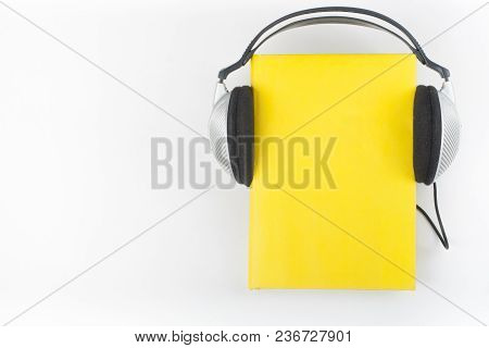 Audiobook On White Background. Headphones Put Over Yellow Hardback Book, Empty Cover, Copy Space For