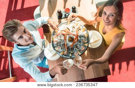 High-angle view of a happy young couple toasting with champagne during romantic dinner with fresh seafood at a trendy restaurant