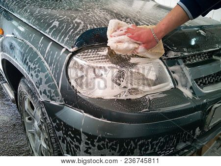 Car Wash. The Worker Washes The Right Headlight With A Sponge And Soap Foam.