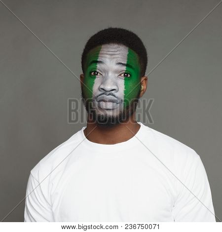 Face Of Young African-american Unhappy Man Painted With Flag Of Nigeria. Football Or Soccer Team Fan