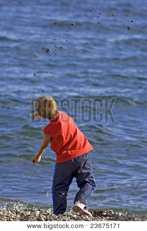 Boy Throwing Pebbles Into The Blue Sea
