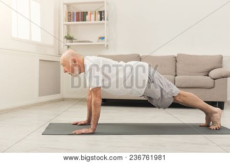 Senior Man Workout At Home. Side View On Mature Caucasian Guy Making Plank Or Push Ups Exercise. Act