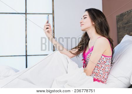 Beautiful Girl In Bed Makes Selfie On Window Background