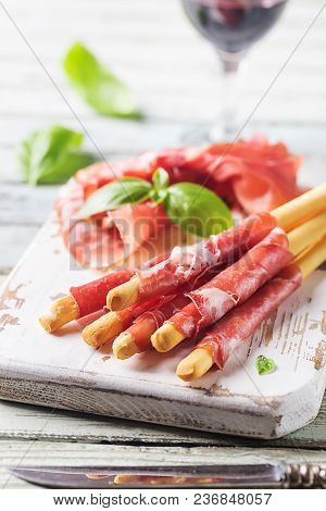 Bread Sticks Grissini With Prosciutto Ham On Cutting Board Over Wooden Background, Close Up