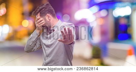 Middle age man, with beard and bow tie stressful and shy keeping hand on head, tired and frustrated at night club