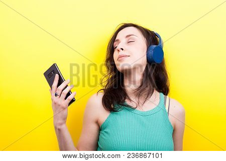 Dreammy Young Woman Listening To Music With A Smartphone In Hands On Yellow Background In Studio