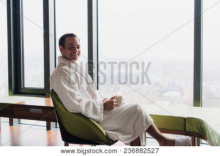 Young Handsome Carefree Man Near Modern Full Length Window Enjoying A Cup Of Coffee While Looking Ou