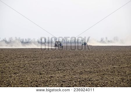 The Tractor Harrows The Soil On The Field And Creates A Cloud Of Dust Behind It.