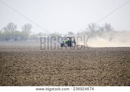 The Tractor Harrows The Soil On The Field And Creates A Cloud Of Dust Behind It.