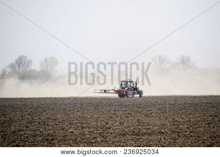 The Tractor Harrows The Soil On The Field And Creates A Cloud Of Dust Behind It.