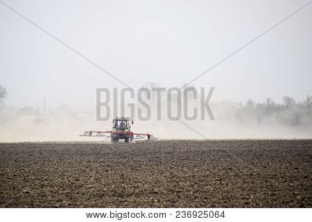 The Tractor Harrows The Soil On The Field And Creates A Cloud Of Dust Behind It.