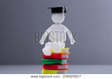Human Figure With Graduation Hat Sitting On Multi Colored Stacked Books