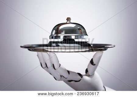 Robotic Hand Holding Service Bell In Plate Against Grey Background