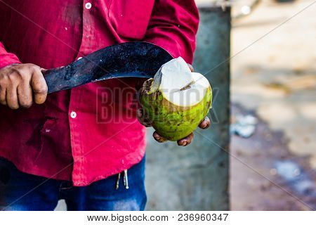 Seller Cutting A Raw Coconut Shell With Sickle To Take Out Coconut Water.