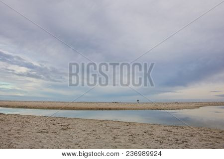 Man Walking On A Beach With Water Reflecting The Soft Colours Of The Sky On Paarden Eiland Beach At 