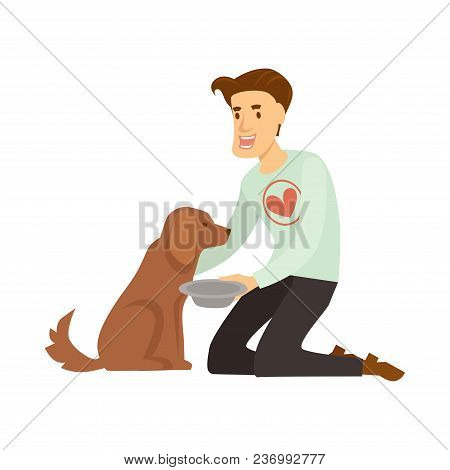 Volunteer In Sweater With Red Heart Feeds Fluffy Homeless Dog. Guy Helps Poor Hungry Animal. Man Hol