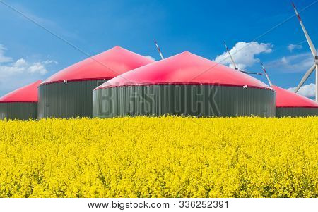 Biogas Plant Stands Behind A Rape Field With Blue Sky