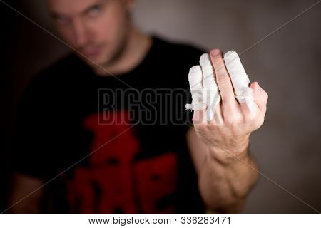 A Man From The Darkness Shows A Hand With Bandaged Fingers, The Middle Finger Is Not Bandaged, The G