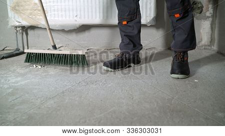 A Worker Is Cleaning A Concrete Floor. Preparing The Floor For Cover. The Hand Of A Working Man Hold